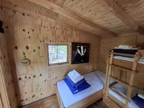 A wooden cabin room with a bunk bed, a window, and a wall-mounted picture.
