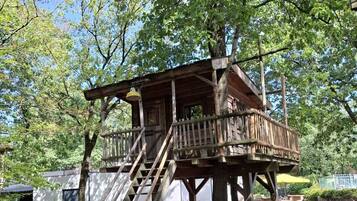 A wooden treehouse with a staircase, surrounded by trees and a clear sky.