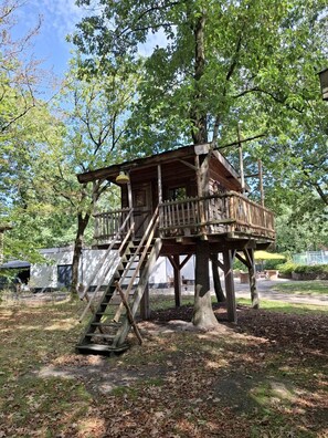 A wooden treehouse with a staircase, surrounded by trees and a clear sky.