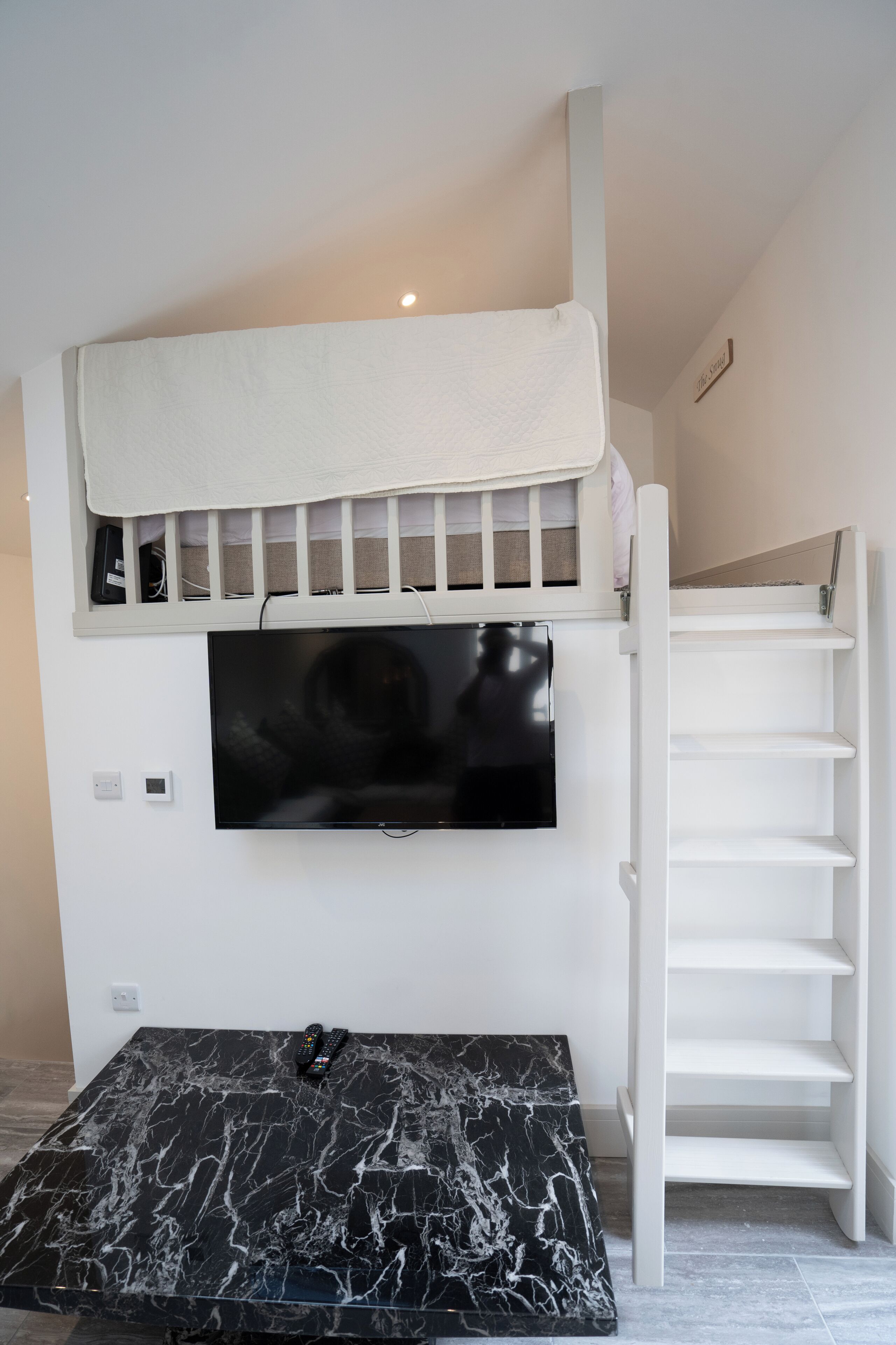 A room with a TV mounted on a white wall, a black marble coffee table, and a white staircase.