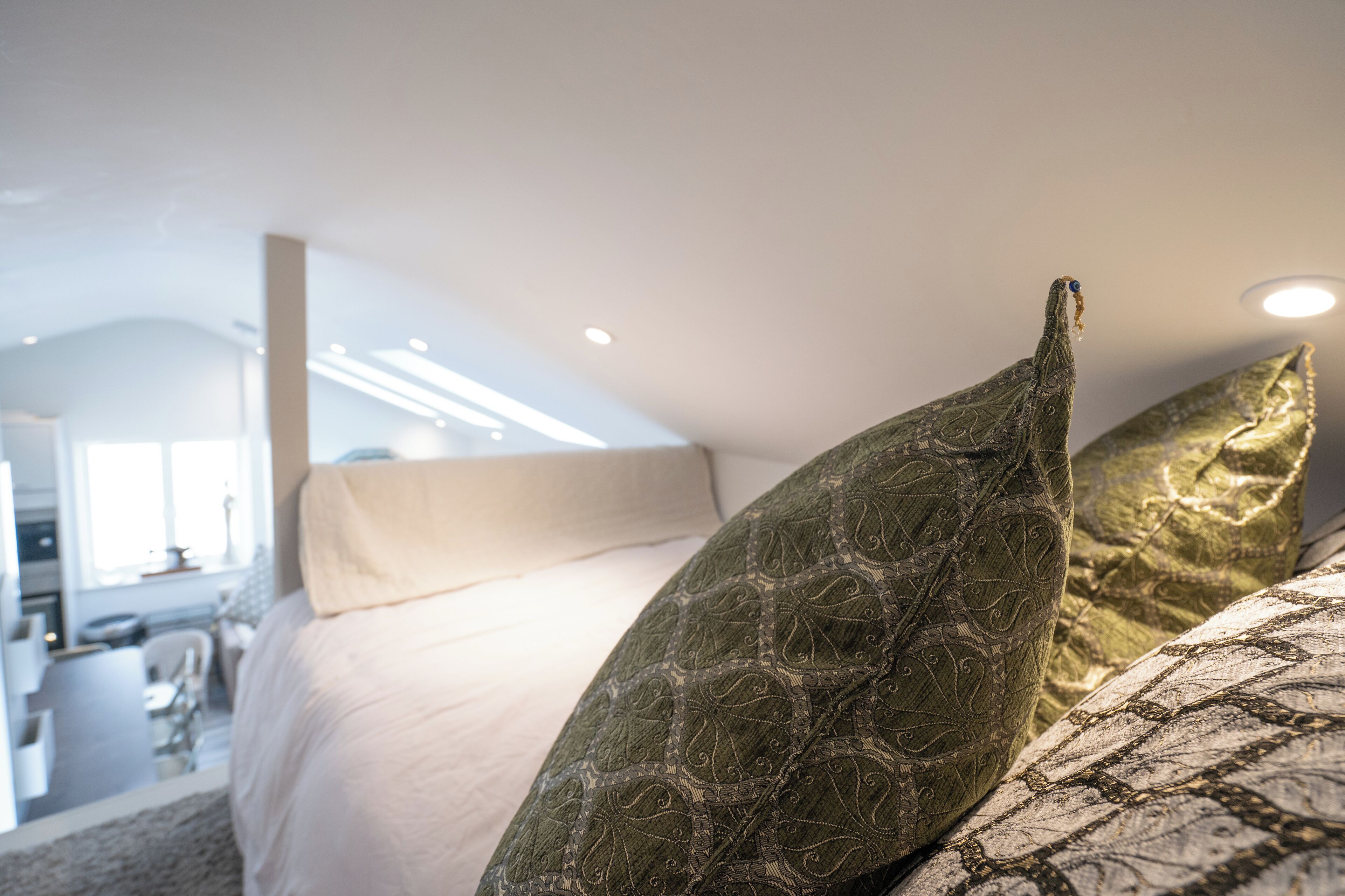 Een slaapkamer met een bed, kussens en uitzicht op een badkamer en een keuken.