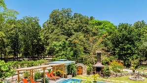 A swimming pool with a stone structure, a wooden pergola, and a stone fireplace surrounded by lush greenery. - Buendía Lux - Piña Suite. Retreat to enjoy the natural beauty of Costa Rica. (Potrero Beach, Tempate)
