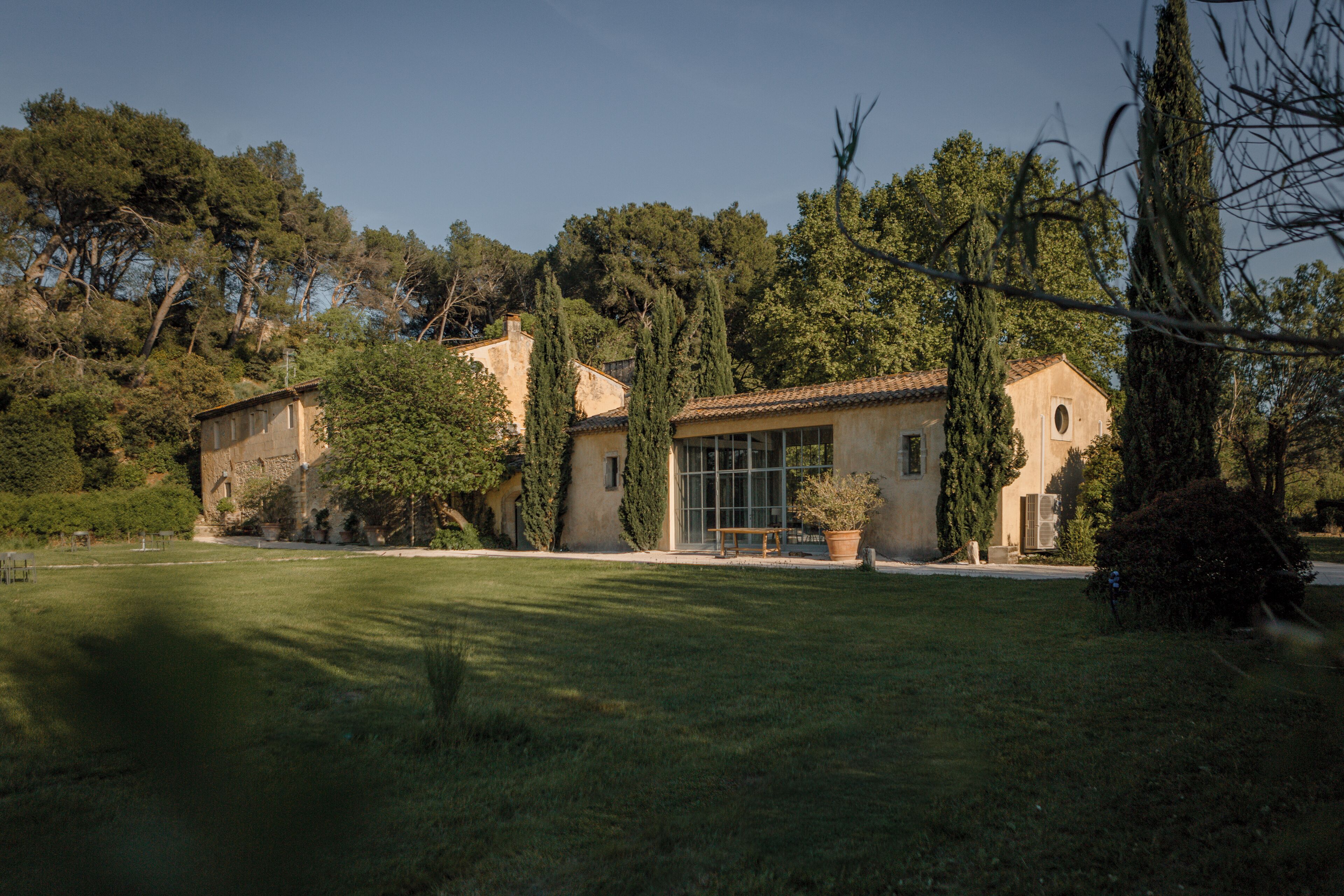 A traditional Mediterranean-style villa with a spacious lawn, a wooden bench, and a large window overlooking the garden.