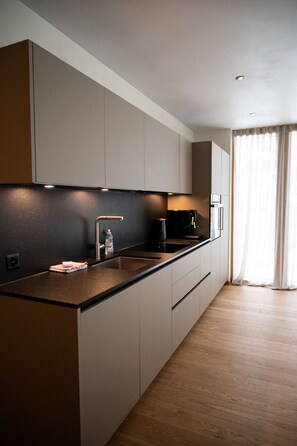 Una cocina moderna con encimera oscura, armarios blancos y suelo de madera.