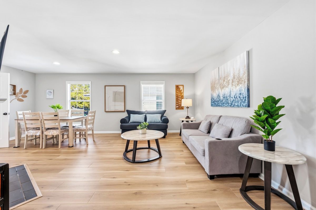 A modern living room with a dining area, a grey sofa, a round coffee table, and a potted plant.