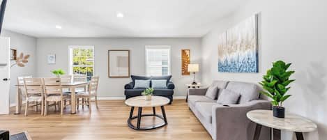 A modern living room with a dining area, a grey sofa, a round coffee table, and a potted plant.