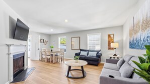 A living room with a fireplace, a grey sofa, a round coffee table, and a TV mounted on the wall. - Beach Square 3 –optional BIKES – Walk 2 Redfern Village, shops, and restaurants! (St. Simons Island)