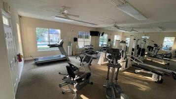 Een sportschool met diverse fitnessapparaten, grote ramen en een plafondventilator.