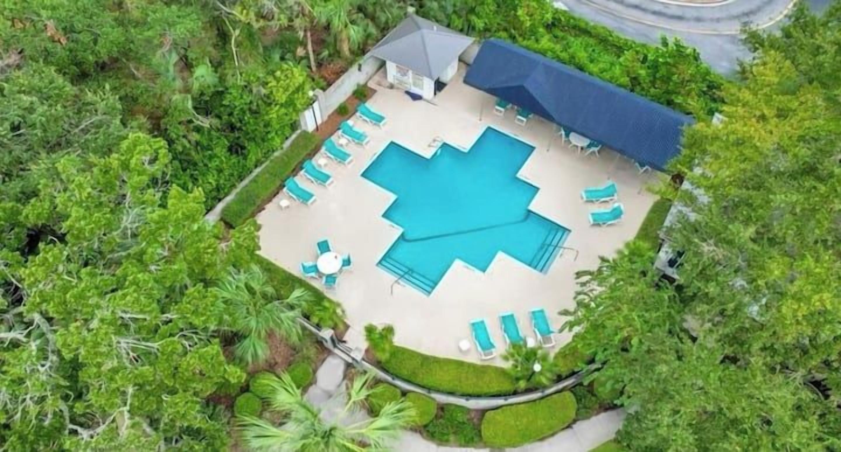 Vue aérienne d’une propriété dotée d’une piscine, de chaises longues et d’un patio couvert, le tout entouré de verdure.