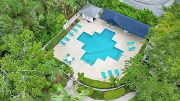 Vue aérienne d’une propriété dotée d’une piscine, de chaises longues et d’un patio couvert, le tout entouré de verdure.