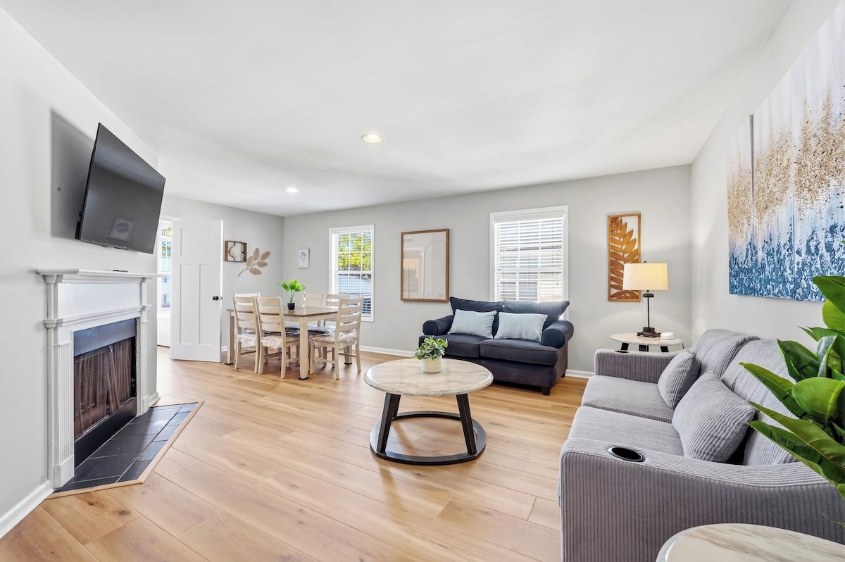 A living room with a fireplace, a sofa, a dining table with chairs, and a TV mounted on the wall.