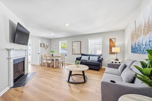 A living room with a fireplace, a sofa, a dining table with chairs, and a TV mounted on the wall.