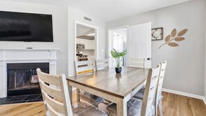 A dining area with a wooden table, chairs, a potted plant, and a television above the fireplace. - Beach Square 3 –optional BIKES – Walk 2 Redfern Village, shops, and restaurants! (St. Simons Island)