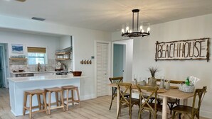 A modern kitchen with a central island, wooden dining table with chairs, and a chandelier. - Waterfront Escape - Beach + Golf Cart + Family Memories - Indian Rocks Beach, FL (Indian Rocks Beach)