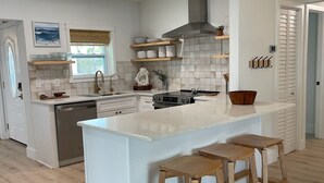 A modern kitchen with a large island, wooden stools, and a view of the ocean through the window. - Waterfront Escape - Beach + Golf Cart + Family Memories - Indian Rocks Beach, FL (Indian Rocks Beach)
