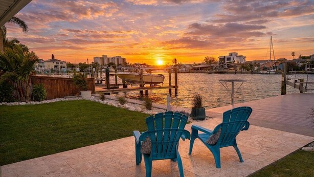 A patio with chairs and a table, overlooking a body of water with boats and buildings in the background. - Waterfront Escape - Beach + Golf Cart + Family Memories - Indian Rocks Beach, FL (Indian Rocks Beach)