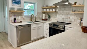 A kitchen with white cabinetry, a stainless steel dishwasher, a built-in oven, and a window with a view of the outdoors. - Waterfront Escape - Beach + Golf Cart + Family Memories - Indian Rocks Beach, FL (Indian Rocks Beach)