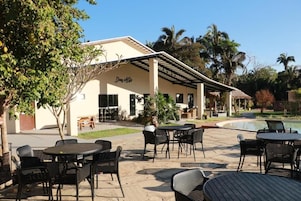Un patio al aire libre con mesas y sillas redondas, una piscina y un edificio con la leyenda "Dom. Ado".