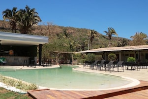 Zona de piscina con sillones de descanso y un edificio de techo plano.