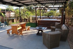 Un patio al aire libre con mobiliario de madera, que incluye una mesa y bancos, además de sofás de mimbre.