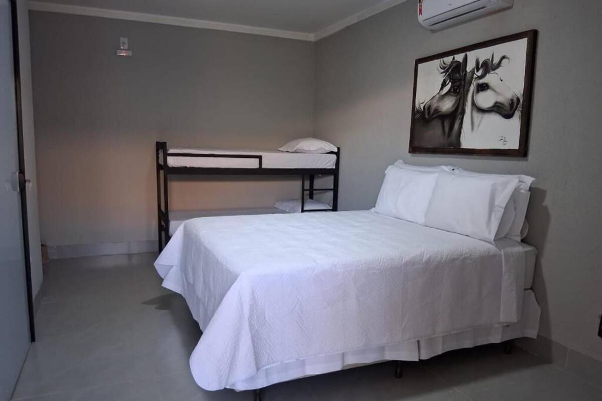 Une chambre avec un lit superposé, un lit simple, un bureau et un climatiseur fixé au mur.