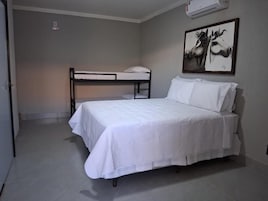 Un dormitorio con una cama nido, una cama individual, un escritorio y un aire acondicionado de pared.