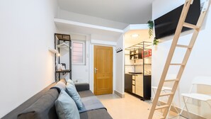 A compact living space with a sofa, a wooden door, a kitchen area, and a ladder. - M (IRI70) Cozy Duplex in the Salamanca district (Madrid)