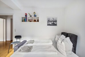 A minimalist room with a bed, a grey sofa, a small table, and a shelf with books and figurines. - Dream on the Old Town Island (Lübeck)