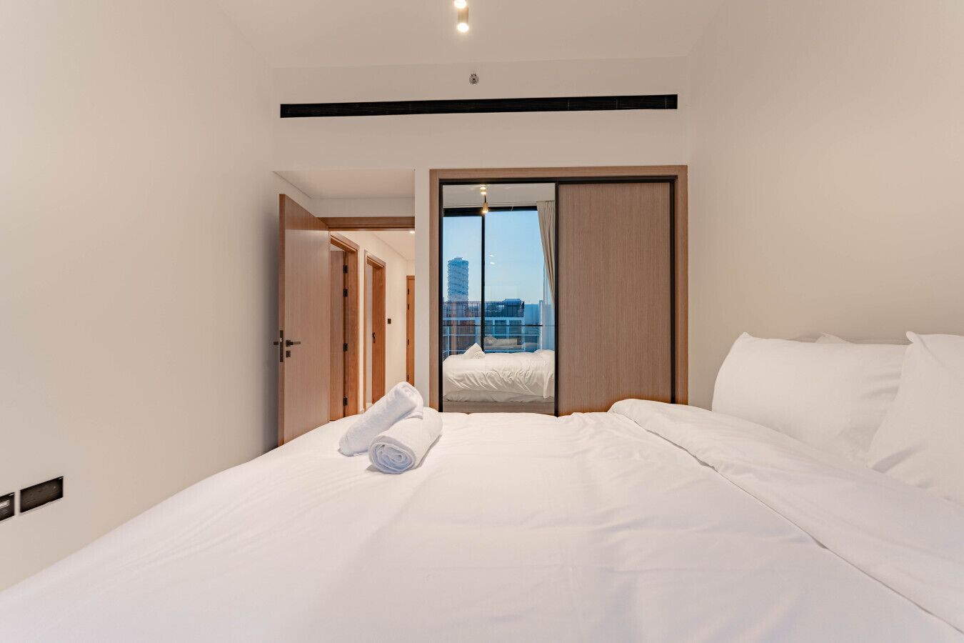 A modern hotel room with a large bed, a view of the city, and a sliding door leading to a balcony.