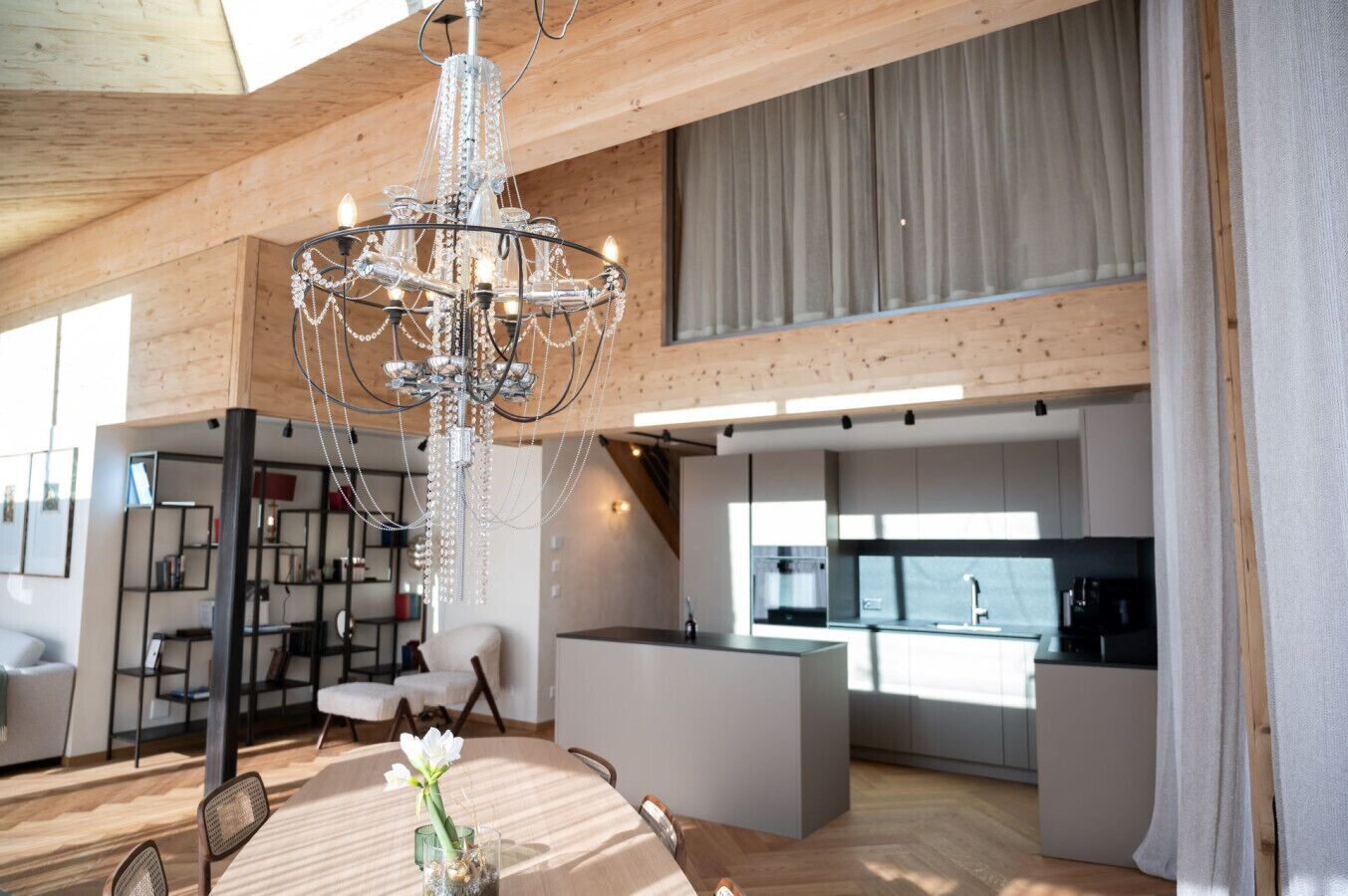 Un'ampia zona giorno con un lampadario moderno, soffitto in legno e vista sulla cucina.