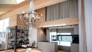 Ampla sala de estar com um lustre moderno, teto de madeira e vista para a cozinha.
