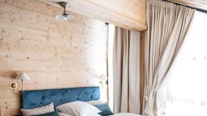 Quarto com painéis de madeira, cama, mesa de cabeceira e janela com cortinas.