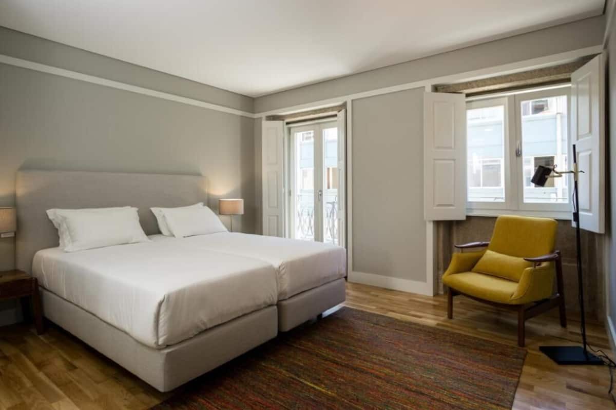 Un dormitorio con una cama doble, una silla y una ventana con cortinas.