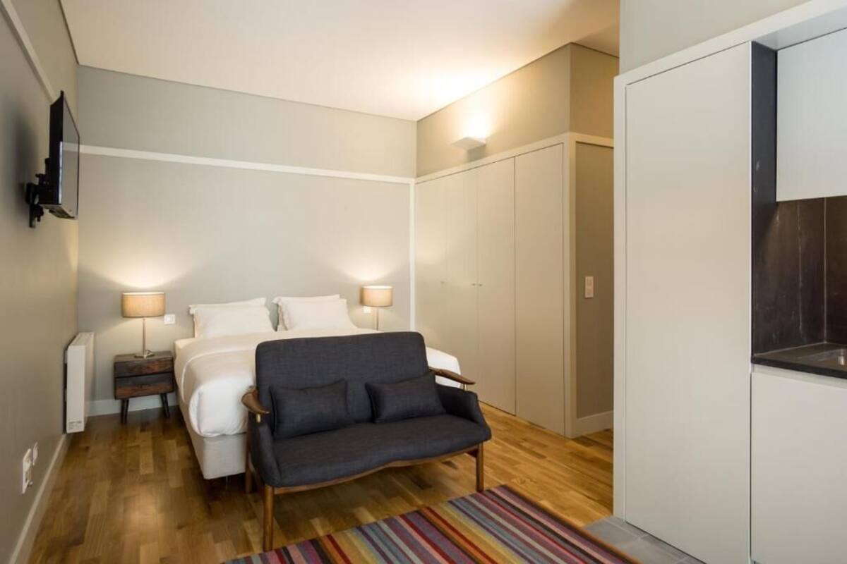 Habitación de hotel compacta con cama, sofá, televisor montado en la pared y armario.