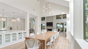 A spacious kitchen with white cabinetry, a long wooden dining table, wicker chairs, and pendant lighting. - Private Marshfront Oasis w/ Pool & Sunset Views (Hilton Head Island)