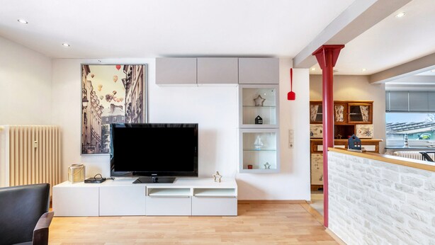 A modern living room with a flat-screen TV, white cabinetry, a red accent column, and a cityscape artwork. - Apartment 'Seestern' with Balcony and Wi-Fi (Wester-Ohrstedt)