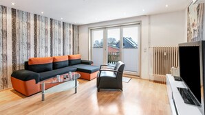 A modern living room with a sectional sofa, a glass coffee table, a black armchair, and a large window with a view of a house. - Apartment 'Seestern' with Balcony and Wi-Fi (Wester-Ohrstedt)