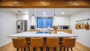 A modern kitchen with a large island, wooden bar stools, white cabinetry, and hanging wooden utensils. - Sleeps 18 - Hot Tub - Playground - Games - Firepit (Broken Bow)
