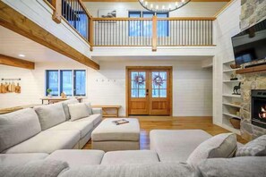 Ein geräumiges Wohnzimmer mit hoher Decke, einem Holzbalkon, einem Kamin und einem großen Fenster.
