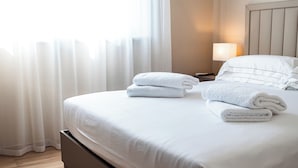 A neatly made bed with white linens and towels, a bedside lamp, and a wooden floor. - D'Stay (Bari)