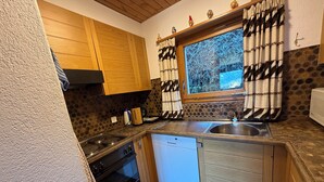 Une cuisine avec des meubles de rangement en bois, une cuisinière, un lave-vaisselle et une fenêtre avec des rideaux.