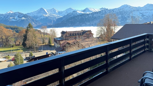 Un balcon offrant une vue sur des montagnes enneigées, un lac et une ville aux bâtiments traditionnels.