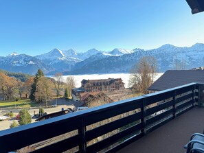Un balcón con vistas a montañas nevadas, un lago y un pueblo con edificios tradicionales.