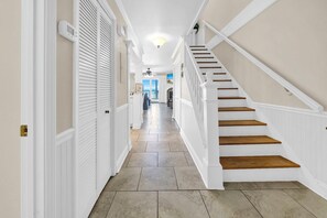 A hallway with a staircase, white walls, and a tiled floor.