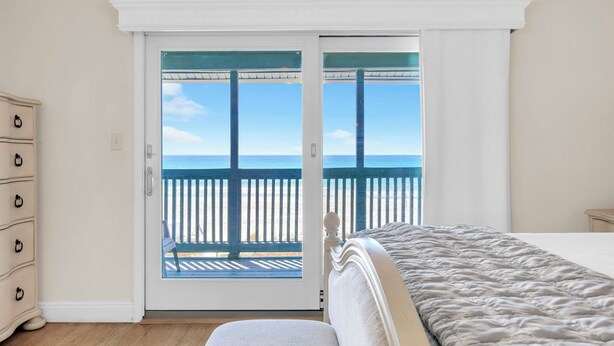 Ein Schlafzimmer mit Bett, Schminktisch und einer Glasschiebetür, die auf einen Balkon mit Meerblick führt.