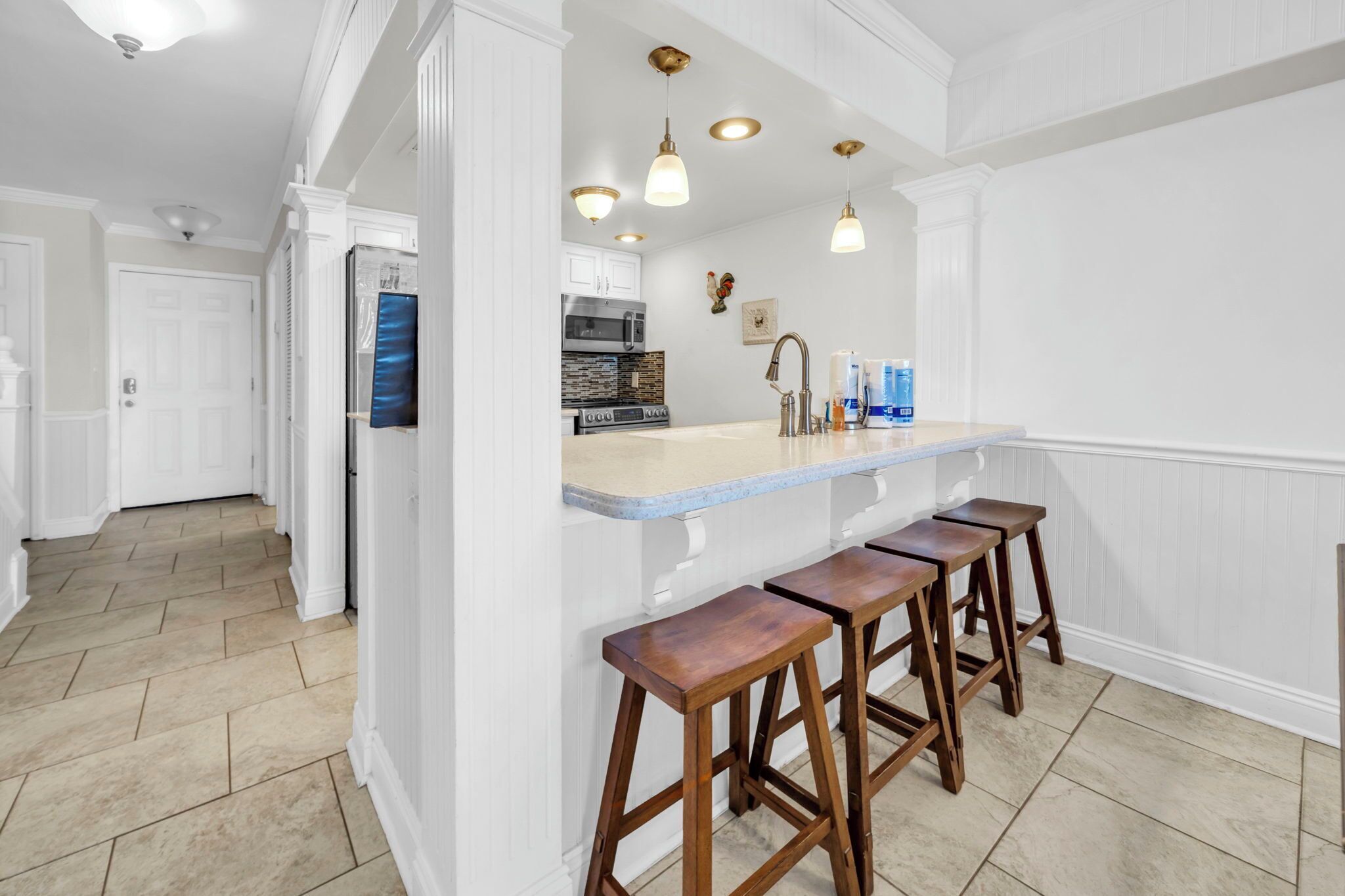 A kitchen with white cabinetry, a marble countertop, and wooden stools.