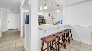 A kitchen with white cabinetry, a marble countertop, and wooden stools.