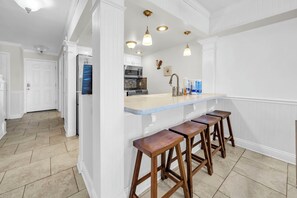 A kitchen with white cabinetry, a marble countertop, and wooden stools.