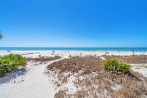 A beach with clear skies, sandy dunes, and a few beach chairs and umbrellas.
