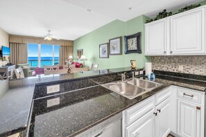 A kitchen with granite countertops, white cabinets, a double sink, and a view of the ocean. - 🏖️Large Balcony with Stunning Gulf Views | Pool | Calypso 2-404🏖️ (Panama City Beach)